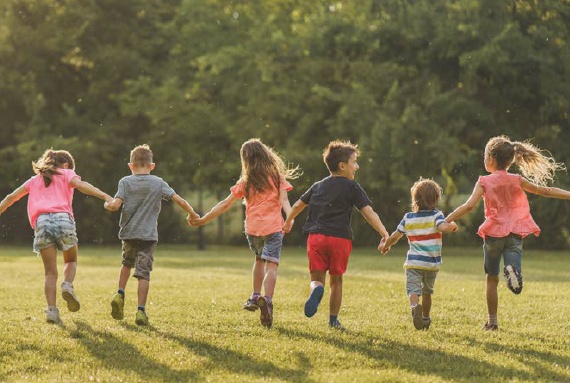 Kinder geben sich die Hände und laufen über eine Wiese (von hinten abgebildet)